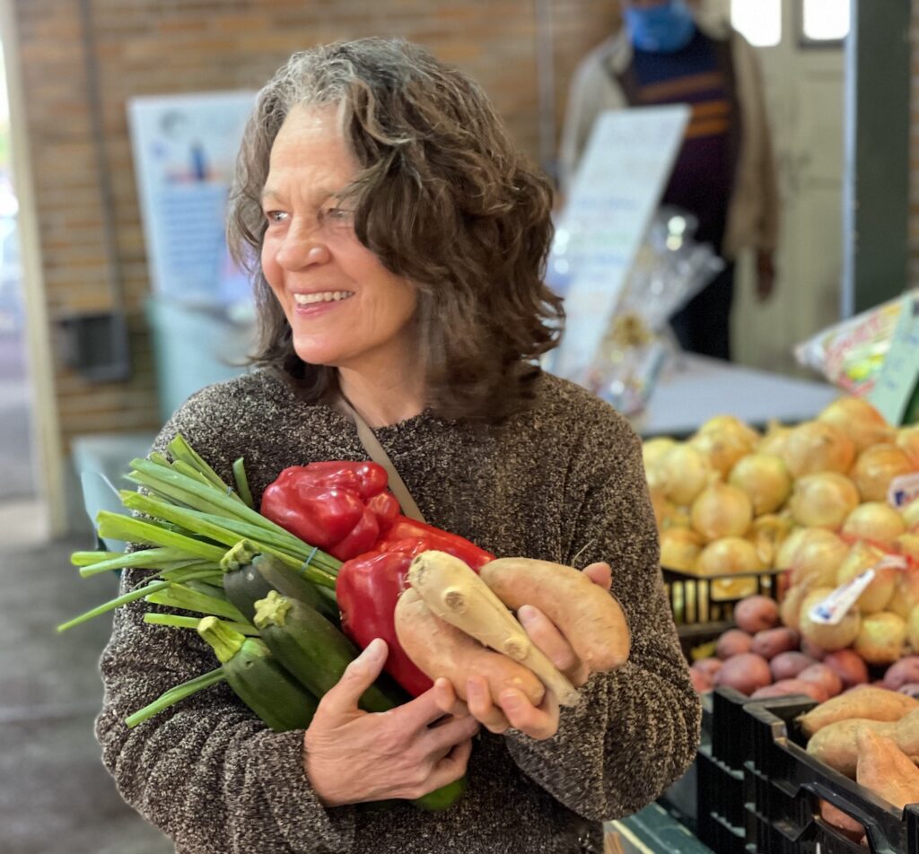 Vegan Storyteller Jeanette McDermott holding an armful of vegetables at a farmers market in St. Louis