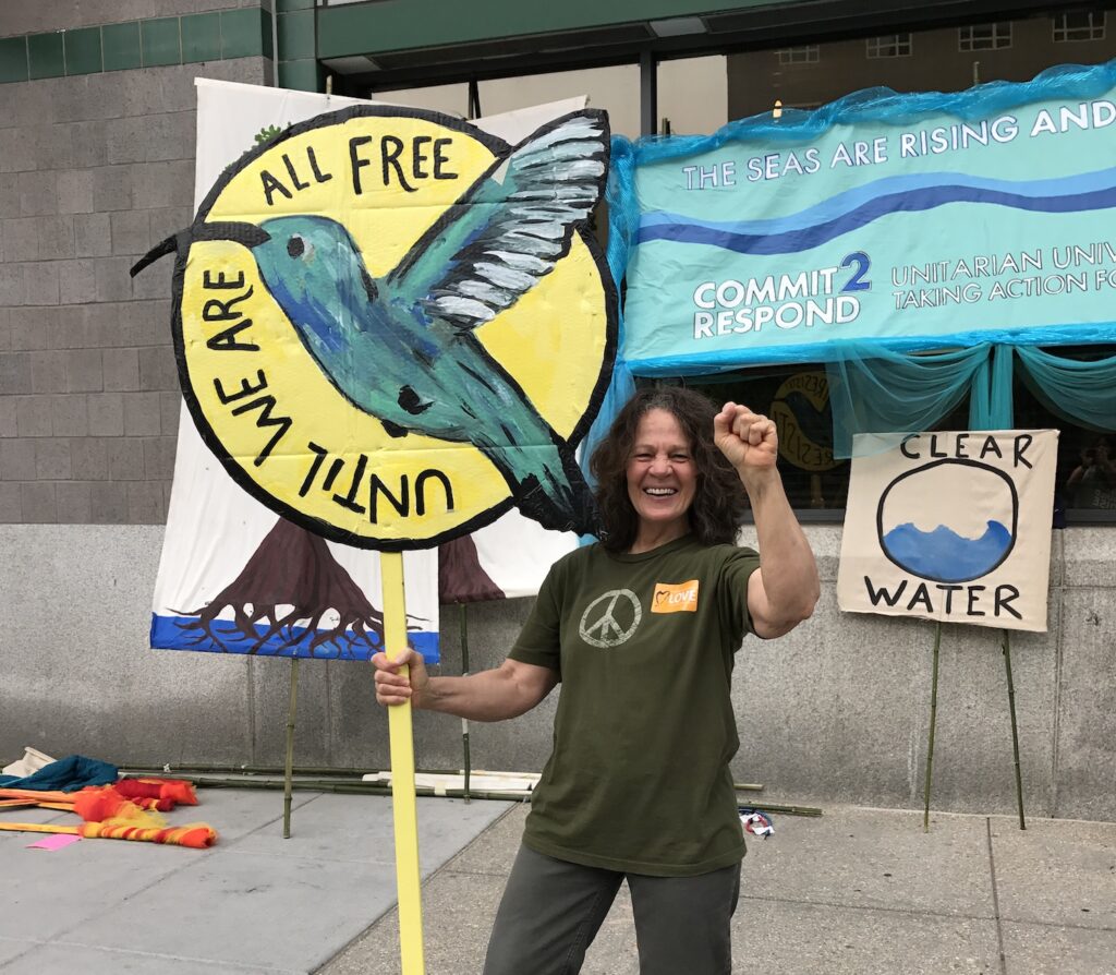 About Vegan Storyteller - Jeanette McDermott at a protest march in Washington DC holding a sign that says Until We Are All Free