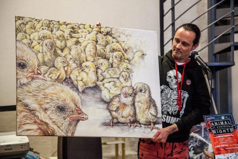 Vegan ARTivist Philip McCulloch-Downs holding a large painting of baby chicks crammed together on a factory farm