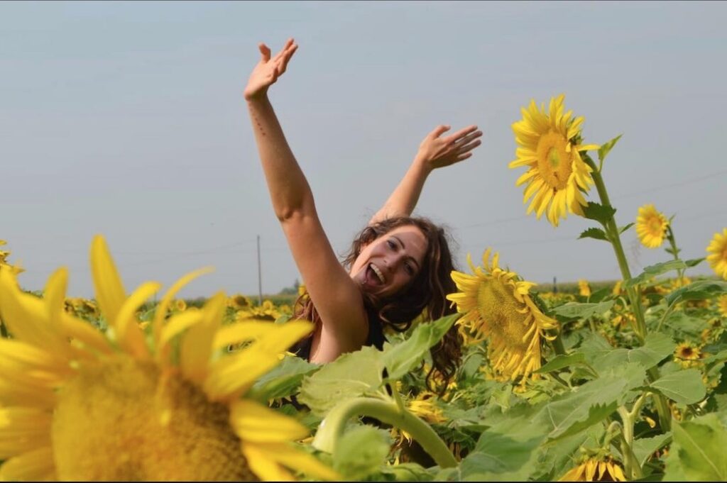 Revers-Lab in a field of sunflowers with her arms raised to the sky