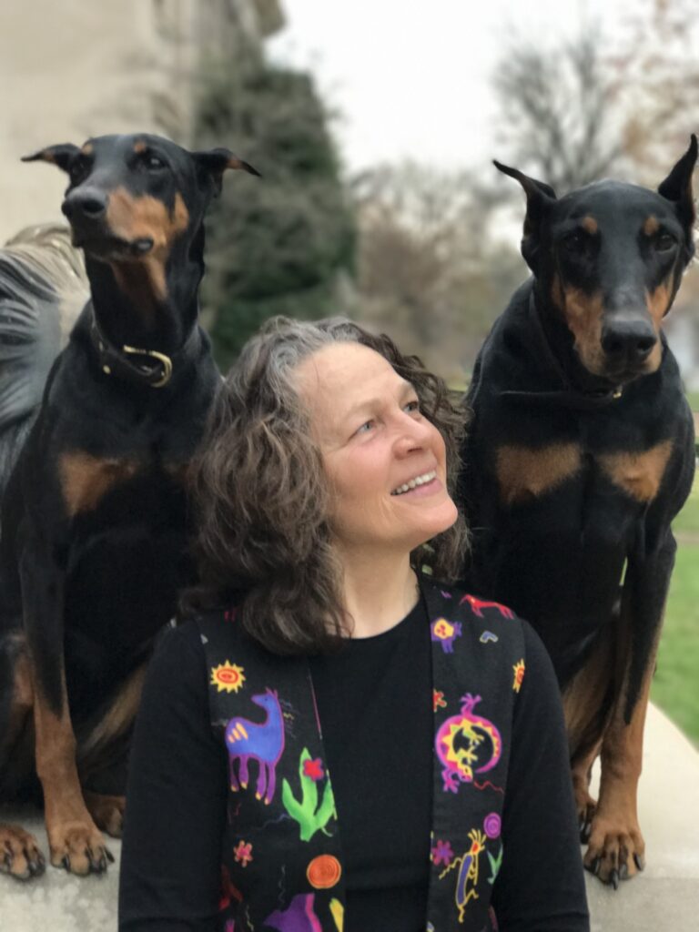 Vegan Storyteller Jeanette McDermott standing between two doberman pinschers
