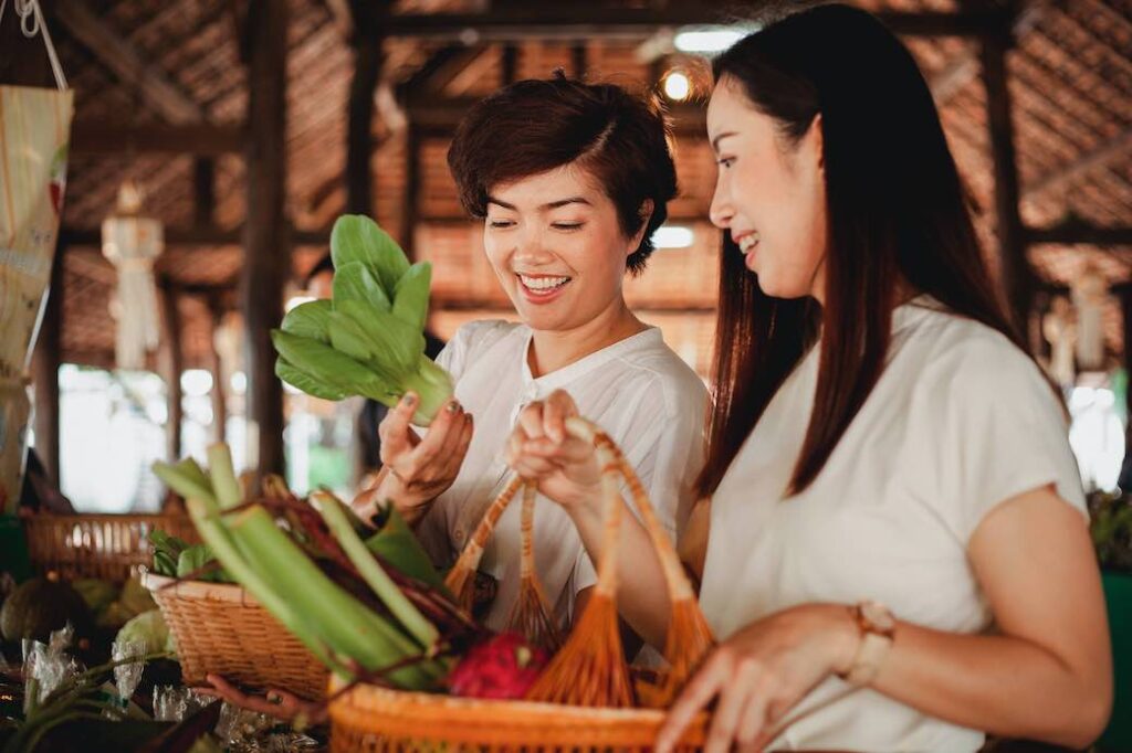 Two Asian women shop as beginner vegans at a vegetable market